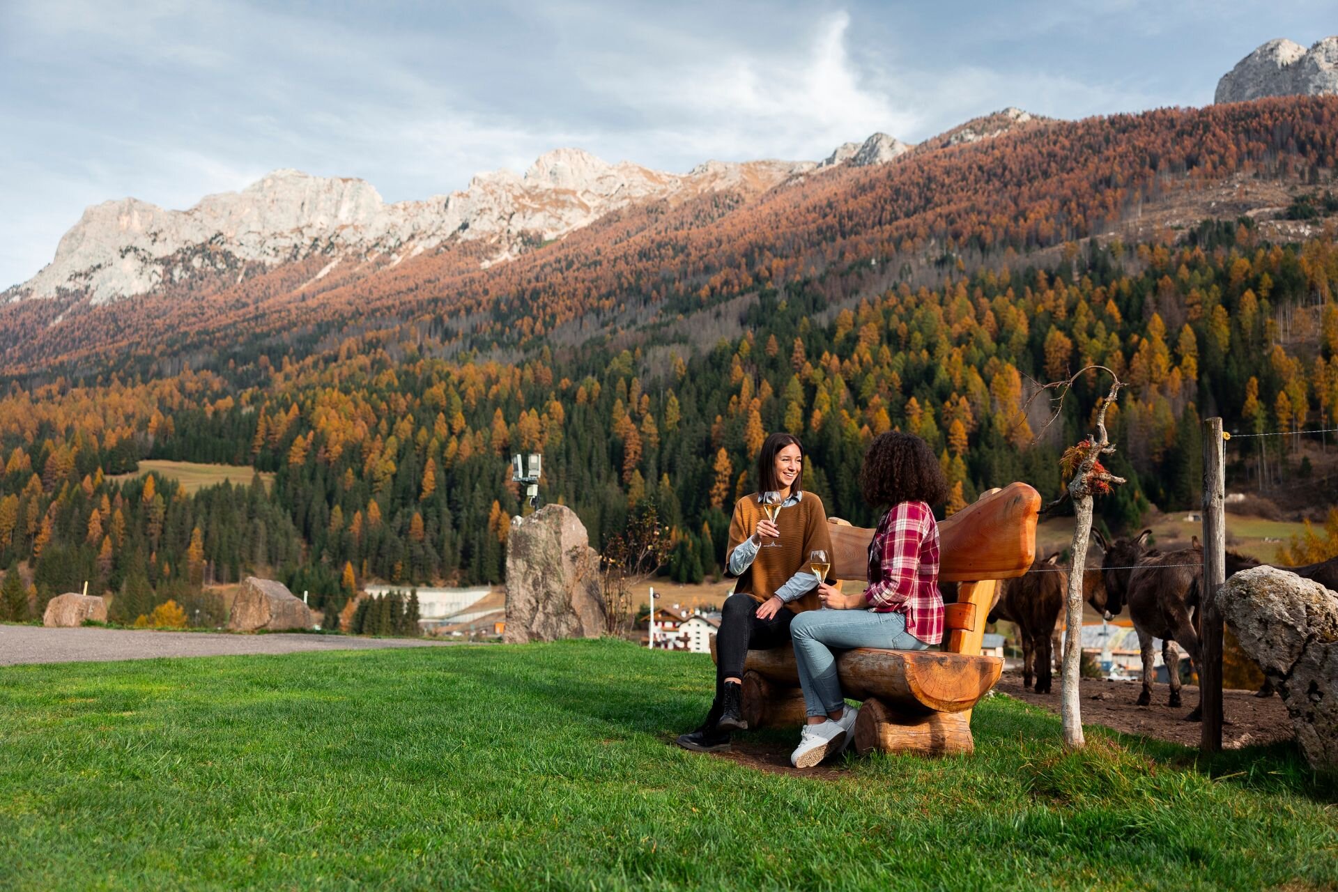 Coppia seduta su una panchina di una malga beve con le dolomiti autunnali sullo sfondo | © Archivio Immagini ApT Val di Fassa - Federico Modica