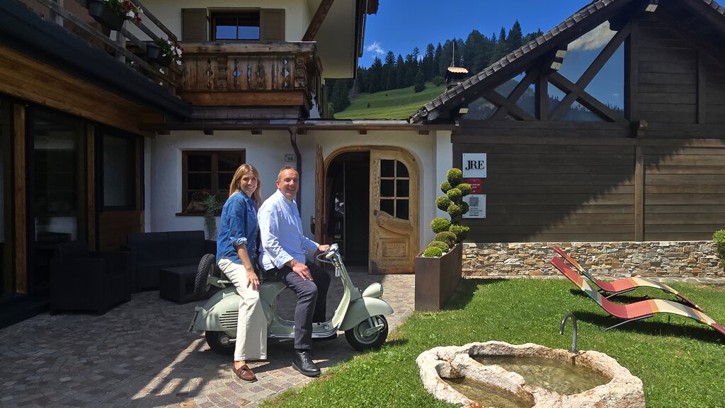 Chiara Maci in sella dello scooter dello chef Paolo Donei davanti alla Malga Panna, Moena